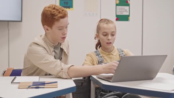 소년의 여학생 책상에 수업을 노트북 컴퓨터를 사용하는 여학생에 이야기하고 있습니다 — 비디오