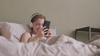 Haftasonu yatağında dinlenirken, kulaklıkla müzik dinleyen rahat, genç bir kadının belden aşağı çekimini yap.