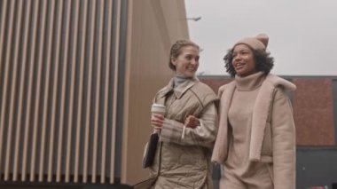 Sonbaharda açık havada yürürken yarı sezonluk kıyafetleriyle sohbet eden iki farklı kadının yavaş çekimleri.