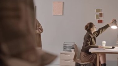 İş gününden önce modern ofiste iş yerlerini düzenleyen, şık günlük kıyafetli iki genç kadının yavaş çekimleri.