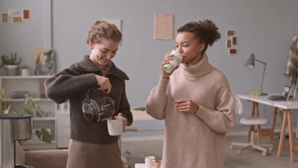 オフィスワークの合間に休憩ドリップコーヒーメーカーからコーヒーを注ぎながらチャット2人の若い多様な女性同僚の中低速ショット — ストック動画