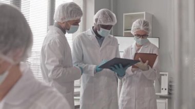 Erkek, çift ırklı ve Afrikalı Amerikalı ve beyaz bilim adamları laboratuarın penceresinde dikilip konuşuyorlar.