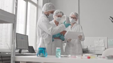 Çift ırklı erkek ve beyaz kadın bilim adamlarından oluşan düşük açılı bir ortam. Çalışma üniforması giyen iki kadın gündüz vakti laboratuvarda oturmuş sohbet ediyorlar.