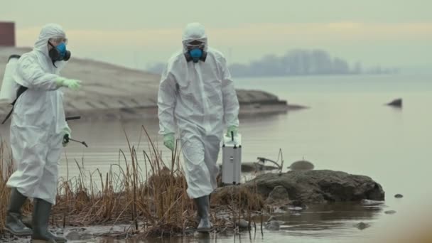 化学訴訟で2人の男性科学者のスローショットや生態系の大惨事が起こった汚染地域の放射性河川の銀行を探索ブーツ — ストック動画