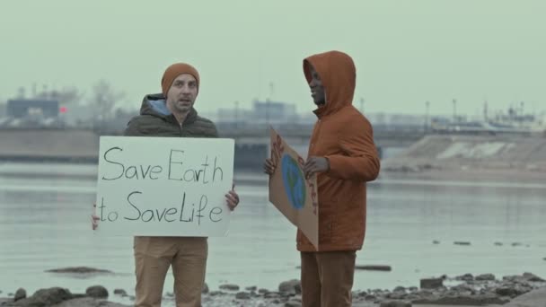 カメラの保護環境でスローガンを叫んでポスターと2人の多様な男性エコ活動家の中低速ショット — ストック動画