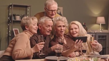 Bir grup mutlu Kafkasyalı son sınıf öğrencisinin kadehleri şarap ve şampanyayla şenlik sofrasında otururken arkadaşlarıyla akıllı telefondan görüntülü konuşma yaparken belini kaldır.