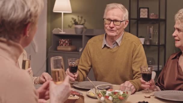 腰アップ遅いですショットの白人シニア男とともに赤ワイン作りトースト座っているお祝いのテーブルで友人ディナーパーティー — ストック動画