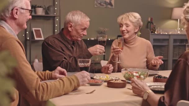 ウエストアップ遅いショットのシニア友人で座っているお祝いのディナーテーブルに自宅で 会話や乾杯のワインとシャンパングラス 一緒に楽しい時間を過ごす — ストック動画
