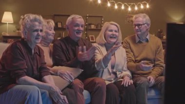 Kanepede oturup TV 'de maç izleyen beş hevesli erkek ve kadının yavaş çekimi.