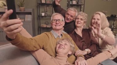Neşeli yaşlıların el kamerasıyla çekilmiş gülümsemeleri ve akıllı telefonlara el sallamaları evde toplanırken arkadaşlarıyla görüntülü konuşma yapmaları.