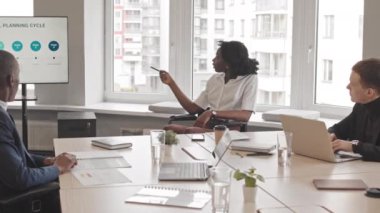 Orta boylu, tekerlekli sandalyede oturan, finans departmanından meslektaşlarına sunum yapan, gündüz vakti masa başında oturan Afrikalı Amerikalı genç bir kadın.