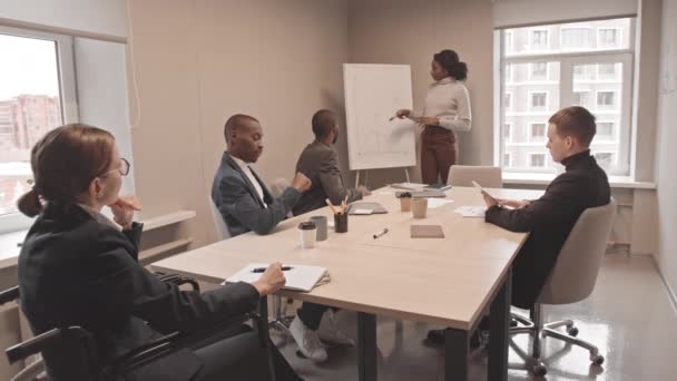 アフリカ系アメリカ人や白人男性や女性の同僚にビジネスグラフを提示若い女性のSteadicam車椅子で昼間の会議室に座って — ストック動画