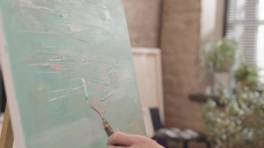 Gündüz vakti sanat stüdyosunda, tanınmayan bir sanatçının elinde sadece çerçeve içinde macun bıçağıyla soyut sanat eserlerini resmetmesi.