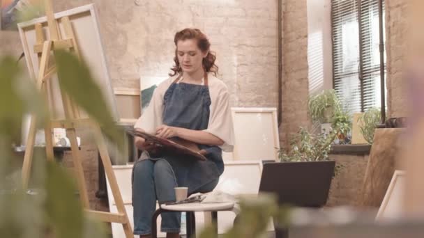 Mediana Largo Joven Mujer Caucásica Con Delantal Sentado Pintando Estudio — Vídeo de stock
