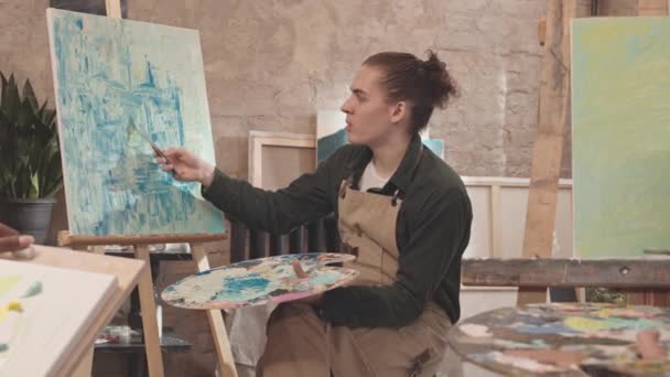 앞치마를 현대적 화실에 캔버스에 그림을 그리며 알아볼 수없는 학생들에게 이야기하는 — 비디오