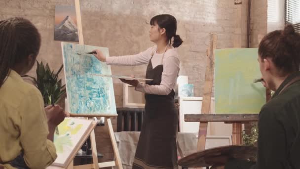 앞치마를 현대적 화실에 캔버스에 그림을 그리고 학생들 이야기하는 — 비디오