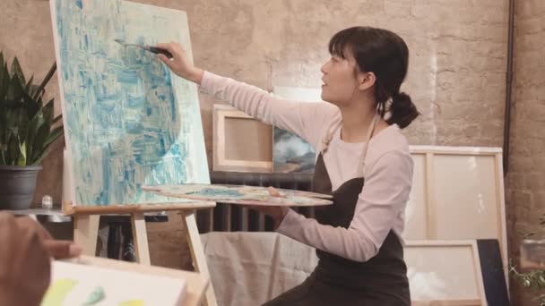 Seguimiento Joven Profesora Arte Asiática Con Delantal Sentada Estudio Moderno — Vídeo de stock