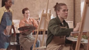 Düşük açılı beyaz adam resim yapıyor. Tablo üzerinde macun bıçağıyla resim yapıyor. Resim sınıfında oturuyor.