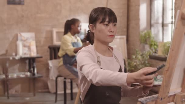 앞치마를 화폭에 나이프로 그림을 그리고 카메라로 즐거운 아시아 여성의 — 비디오