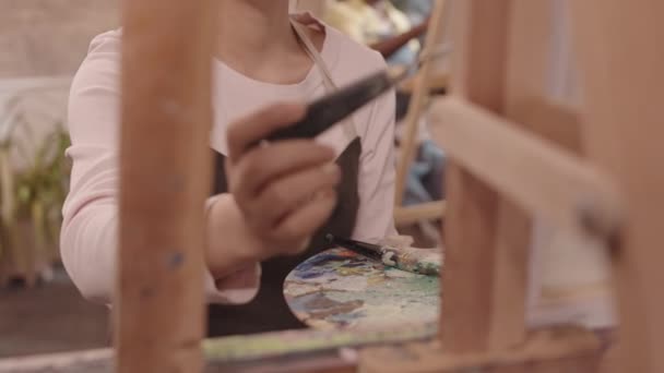 エプロンを身につけたアジア系女子美術生の肩の力を借り スタジオではパティナイフで絵を描く — ストック動画