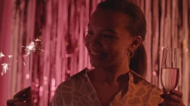 Maytap ve şampanya bardağıyla kırmızı folyo perdeye poz veren güzel, melez bir kadının yavaş yavaş portresi.