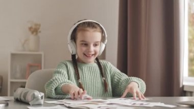 Waist up slowmo shot of cute 5-year-old girl in headphones practicing speech therapy, showing words and letters printed on cards at camera