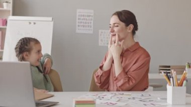 Waist up slowmo shot of 5-year-old girl and female speech therapist practicing correct pronunciation and articulation in classroom