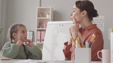 Sınıfta ders sırasında konuşma terapistiyle doğru telaffuz pratiği yapan küçük kızın belden aşağı çekimini yap.