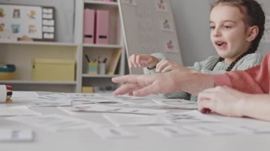 Medium close up with slowmo of 5-year-old girl learning alphabet using printed letters on cards together with female teacher