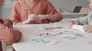 Slowmo shot of two kids learning alphabet at speech therapy lesson with female teacher showing them printed colorful words and letters on cards