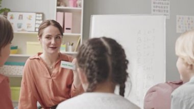 Medium slowmo shot of female speech therapist working with group of children in bright classroom, learning rules of pronunciation together