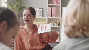Medium slowmo shot of young female speech therapist teaching alphabet to group of children in classroom