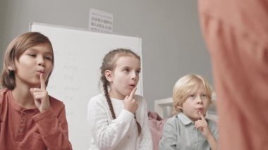 Medium slowmo shot of two boys and girl of elementary age doing articulation exercises with female speech therapist