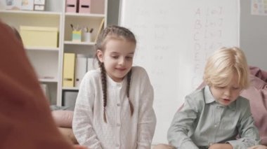 Medium slowmo shot of three Caucasian elementary kids playing with flashcards when learning alphabet with speech therapist
