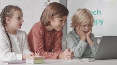 Waist up shot of three Caucasian kids of elementary age studying on laptop in classroom during speech and language therapy