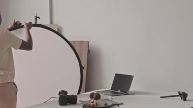 Medium slowmo shot of African-American female food photographer setting up professional lighting in studio before taking pictures of blueberry cheese pancakes on digital camera