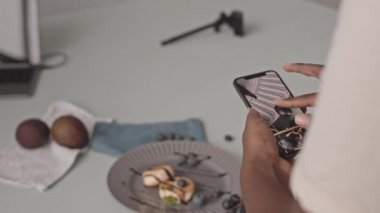 Medium closeup of unrecognizable African-American woman taking pictures of delicious blueberry cheese pancakes on smartphone