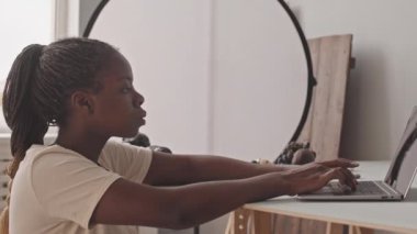 Chest up shot of young African-American female photographer working on laptop in photo studio