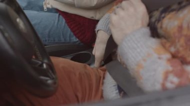 Medium slowmo shot of happy young Caucasian couple fastening seat belts in car before starting ride on winter day