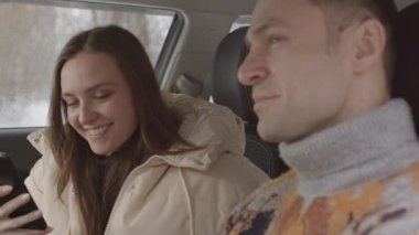 Medium slowmo shot of young Caucasian couple having conversation in car on winter day. Woman taking picture of view from windshield on smartphone