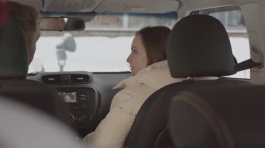 Rear-view slowmo shot of young Caucasian couple talking while sitting in car on winter day
