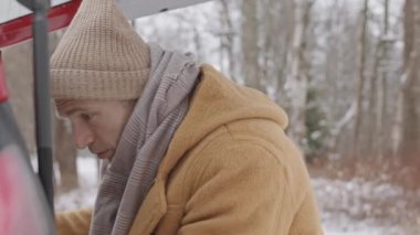 Medium slowmo shot of young Caucasian couple taking their backpacks out of car boot standing in forest on cold winter day