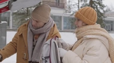 Medium slowmo shot of young Caucasian couple have arrived at their destination of beautiful winter forest by car, taking their backpacks from trunk and starting walk