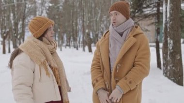 Medium slowmo shot of young Caucasian couple standing in forest on cold winter day having conversation