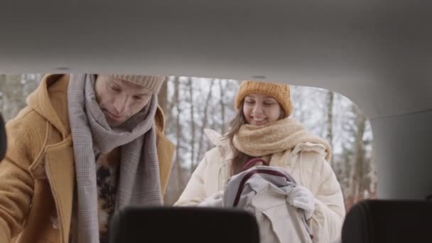 美しい冬の森で週末に到着したときに車のトランクから自分の持ち物を取って若い白人カップルの中低速ショット — ストック動画