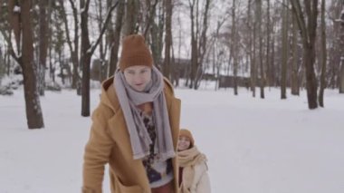 Slowmo shot of cheerful man carrying his girlfriend on sleigh, having fun in winter forest on