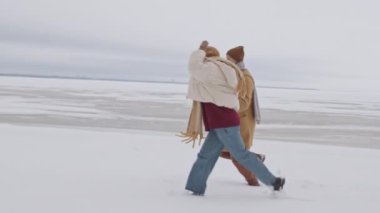 Slowmo shot of young Caucasian couple I love having fun together running along snowy winter beach on cold day