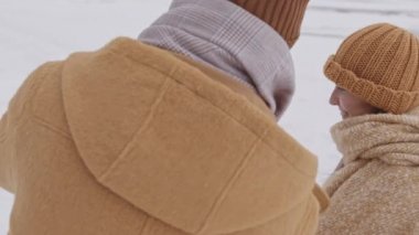 Medium arc shot of young Caucasian couple making snowman together on cold winter day