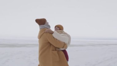 Medium slowmo shot of cheerful young Caucasian couple having fun together outdoors in snow-covered winter landscape