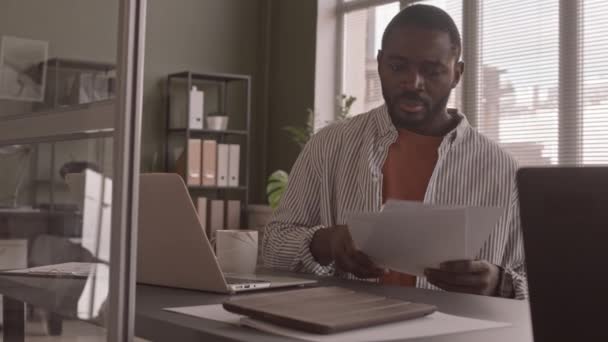 現代のオフィスでラップトップで作業しながら 財務文書を見てアフリカ系アメリカ人ビジネスマンの中低速ショット — ストック動画